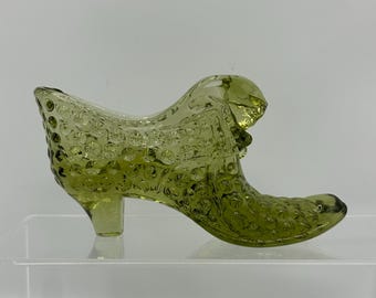 May include: A green glass shoe with a high heel and a textured surface. The shoe is a decorative object.