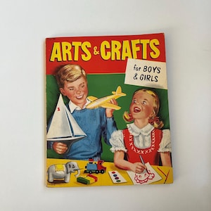 May include: Vintage "Arts & Crafts" book cover featuring two children with craft projects. The cover has a red and green background with the title in yellow. The children are holding a sailboat, airplane, and drawing.