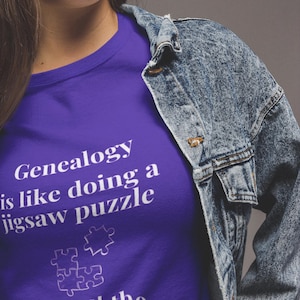 May include: Purple t-shirt with white text that reads "Genealogy is like doing a jigsaw puzzle without the box top". A white jigsaw puzzle piece is pictured above the text.