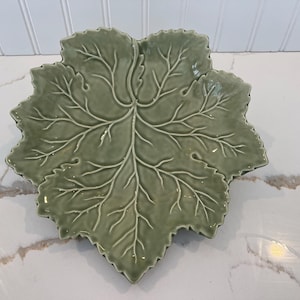 May include: A green ceramic leaf-shaped serving dish. The dish is detailed with raised veins and a textured surface.