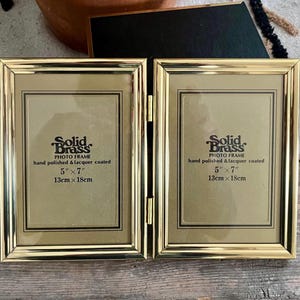 May include: A hinged, gold-colored brass photo frame. Each frame is 5" x 7" (13cm x 18cm) and features the text "Solid Brass PHOTO FRAME hand polished & lacquer coated". The frame is designed to hold two photos.