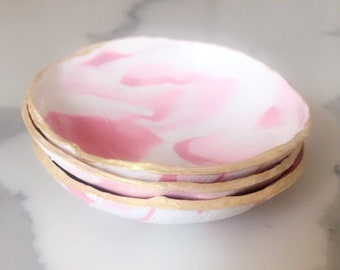 Puede incluir: Tres platos de cerámica apilados de color rosa y blanco con vetas marmoleadas y borde dorado.