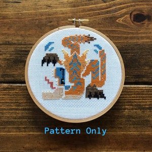 May include: Cross stitch pattern of a colorful dragon with blue, orange, and brown details. The pattern is in a white embroidery hoop with a wooden frame.