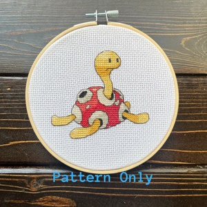 May include: Cross-stitch embroidery of a turtle in a wooden hoop. The turtle has a yellow head and limbs, a red shell with white and black spots. The text "Pattern Only" is printed in blue at the bottom.