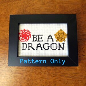 May include: A framed cross-stitch pattern with the words "BE A DRAGON" and two stylized symbols, one red and one gold, on a white background. The text "Pattern Only" is printed below the cross-stitch.