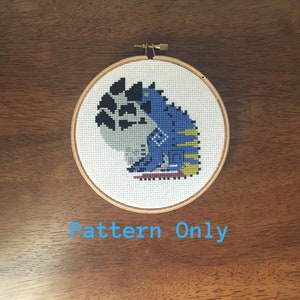 May include: A cross-stitch pattern of a blue and yellow creature with black and white accents, in a wooden embroidery hoop. The text "Pattern Only" is below the hoop.