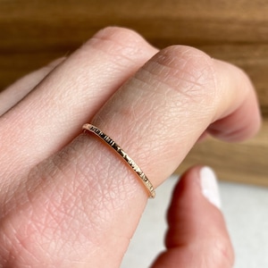 May include: A delicate gold ring with a textured surface. The ring is thin and appears to be worn on a finger. The ring's surface has a series of fine, parallel lines, creating a subtle, tactile pattern. The ring is a simple, elegant piece of jewelry.
