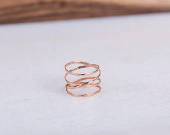 May include: A rose gold ring with a delicate, interwoven design. The ring is made of multiple thin bands that are twisted and intertwined to create a unique and intricate pattern.
