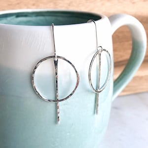 May include: A pair of silver dangle earrings with hammered circle designs. The earrings have a long, thin, hammered bar that hangs from the circle.