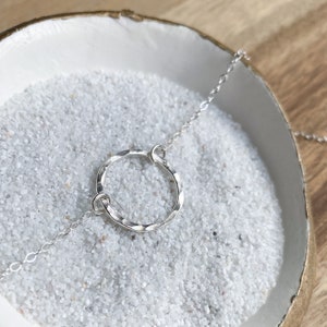 May include: A silver necklace with a hammered circle pendant. The necklace is on a white surface with small white stones.