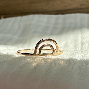 May include: A gold-toned ring with a double-arch design, resembling a rainbow.