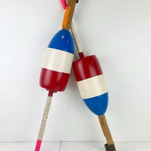 May include: Two decorative buoys in red, white, and blue, with wooden poles and accents. One buoy is red and white, the other is blue and white. The poles have pink and orange details, creating a nautical theme.