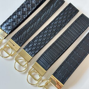 May include: Five black leather keychains with gold metal key rings. Each keychain has a different woven pattern.