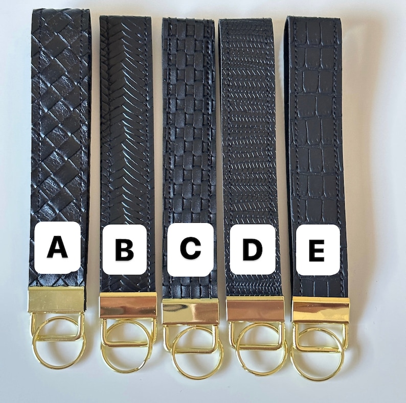 May include: Five black leather keychains with gold key rings. Each keychain has a different pattern: woven, diagonal lines, squares, vertical lines, and crocodile skin. The keychains are labeled A, B, C, D, and E.