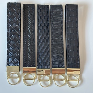 May include: Five black leather keychains with gold key rings. Each keychain has a different embossed pattern.