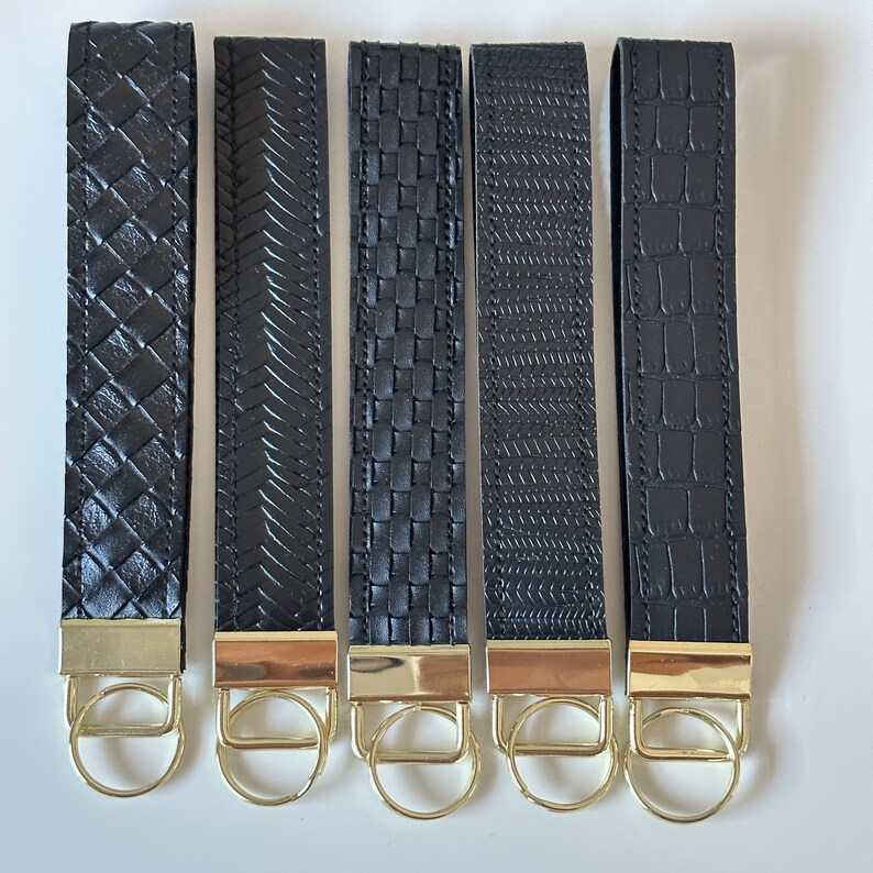 May include: Five black leather keychains with gold key rings. Each keychain has a different embossed pattern.