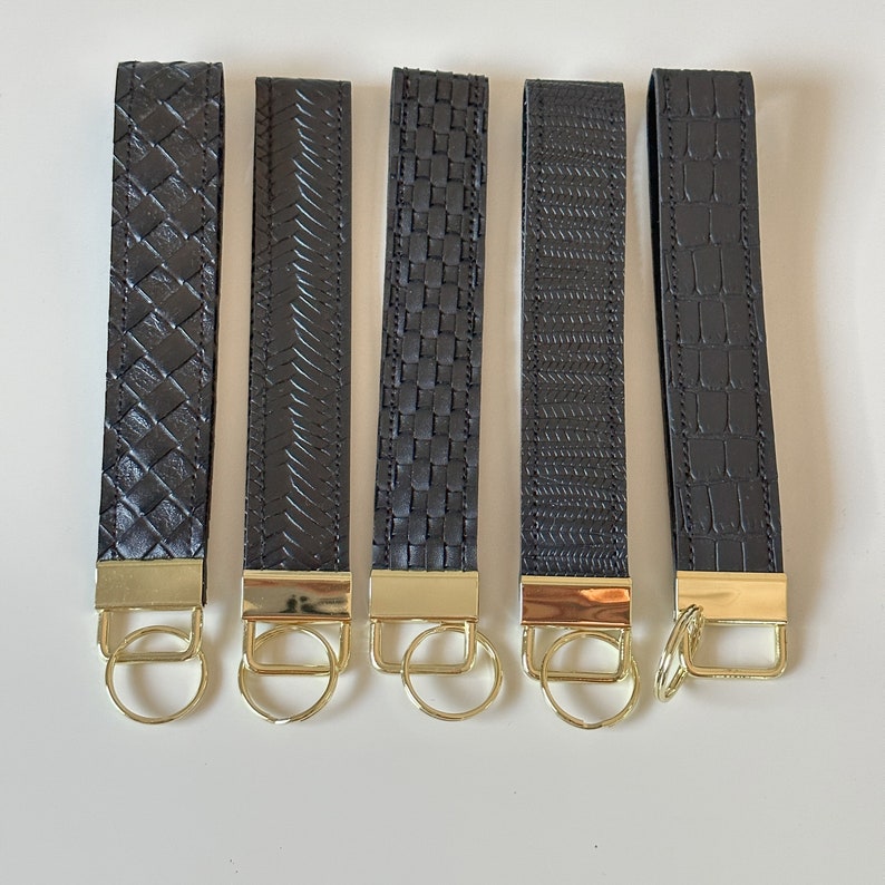 May include: Five black leather keychains with gold metal key rings. Each keychain has a different woven or embossed pattern.