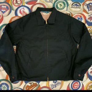 May include: A navy blue jacket with a collared neckline and a gold zipper. The jacket has long sleeves with buttoned cuffs and two front pockets. The interior lining is a red and white checkered pattern.