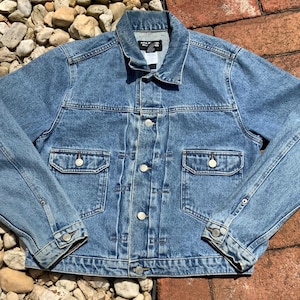 May include: A light blue denim jacket with a button closure, two chest pockets, and two front pockets. The jacket has a classic style and is made of a soft, comfortable material.