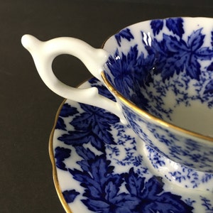 May include: A blue and white teacup and saucer set with a floral pattern. The cup has a white handle and a gold rim. The saucer also has a gold rim.
