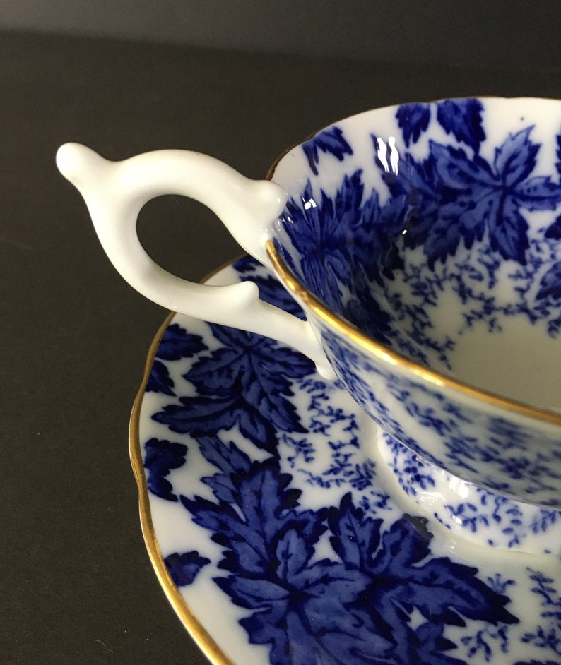 May include: A blue and white teacup and saucer set with a floral pattern. The cup has a white handle and a gold rim. The saucer also has a gold rim.