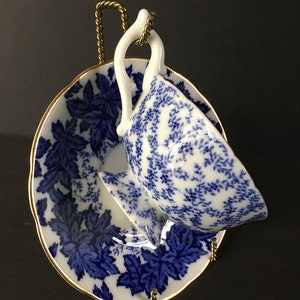 May include: A blue and white porcelain teacup and saucer set with a floral pattern. The cup and saucer are on a gold metal stand.