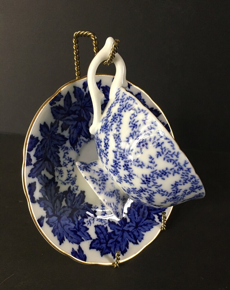 May include: A blue and white porcelain teacup and saucer set with a floral pattern. The cup and saucer are on a gold metal stand.