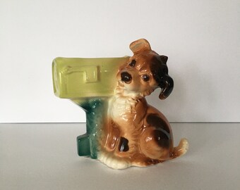 Może przedstawiać: Ceramiczna doniczka w kształcie skrzynki pocztowej z figurką brązowego i czarnego psa siedzącego na górze. Skrzynka pocztowa jest pomalowana na zielono i żółto.