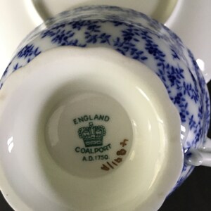 May include: Close-up of the bottom of a white teacup with a blue and white floral pattern. The teacup has a gold inscription that reads "England Coalport A.D. 1750".