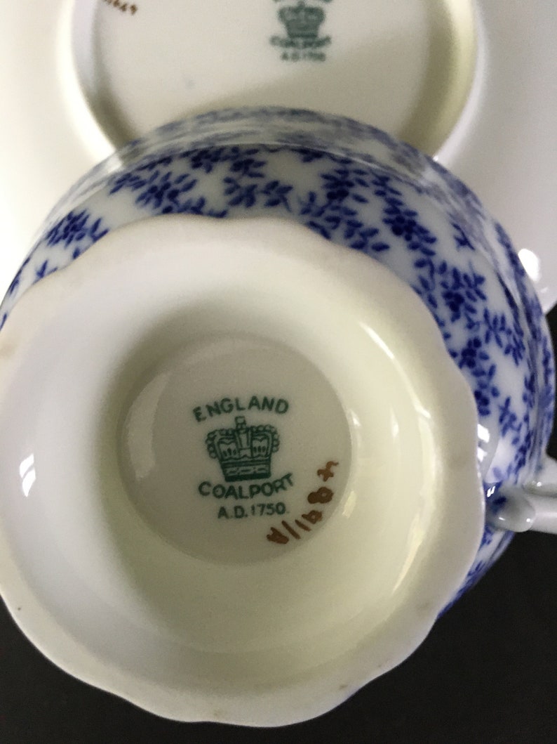 May include: Close-up of the bottom of a white teacup with a blue and white floral pattern. The teacup has a gold inscription that reads "England Coalport A.D. 1750".