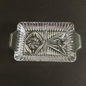 May include: A clear glass divided serving tray with two sections. The tray has a cut glass design and two handles on the sides.