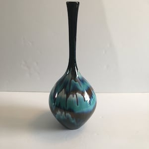 May include: A decorative vase with a dark teal neck and a rounded body. The body has a glossy finish with a blend of teal, brown, and white dripped patterns. The vase's design is artistic and unique. The vase is a decorative item.