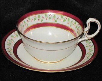 Può includere: Un set da tè bianco con una tazza e un piattino con un bordo bordeaux e oro e un motivo a vite verde.