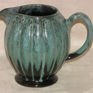 May include: A green and black ceramic jug with a rounded body and a ribbed design. The jug has a wide spout and a handle.