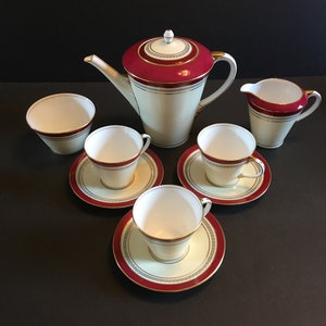 Peut inclure: Un service à thé vintage de couleur crème et rouge avec des finitions dorées et un motif géométrique. L'ensemble comprend une théière, un pot à crème, un sucrier et quatre tasses et soucoupes.