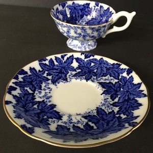 May include: A blue and white teacup and saucer set with a leaf pattern. The saucer has a gold rim.