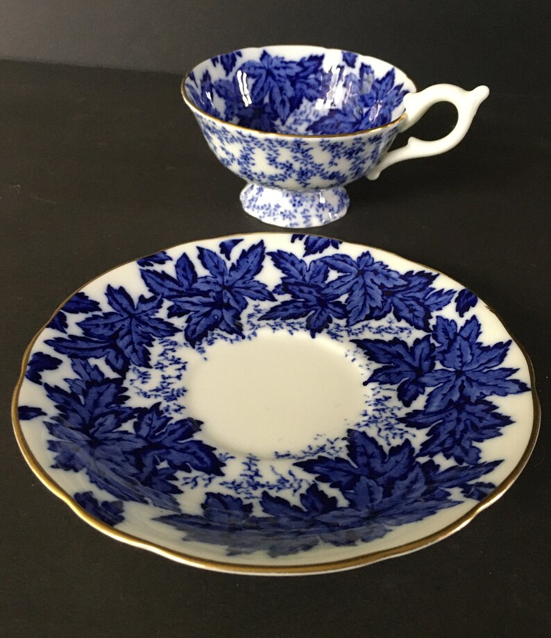 May include: A blue and white teacup and saucer set with a leaf pattern. The saucer has a gold rim.