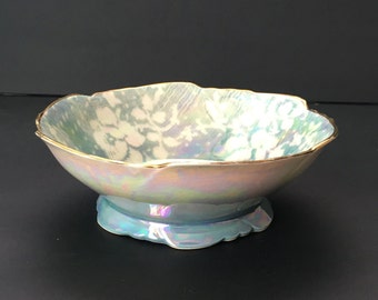 May include: A small, iridescent blue and white bowl with a gold rim and a scalloped edge. The bowl has a pedestal base.