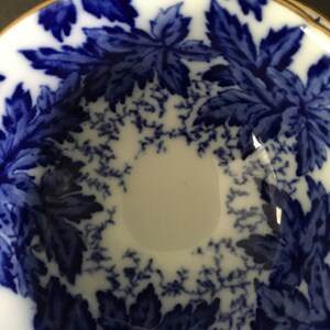 May include: A white ceramic bowl with a blue and white floral pattern. The bowl has a gold rim and is decorated with a repeating pattern of leaves.