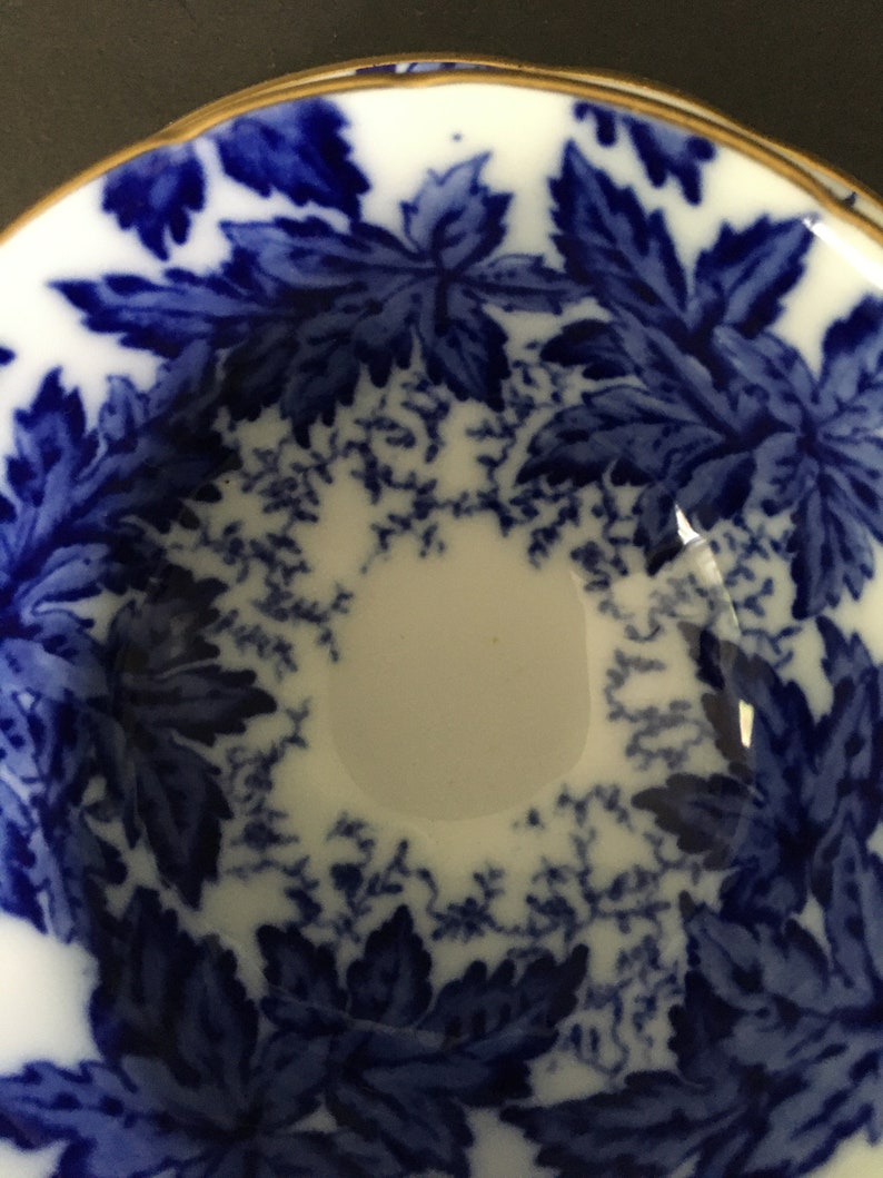 May include: A white ceramic bowl with a blue and white floral pattern. The bowl has a gold rim and is decorated with a repeating pattern of leaves.