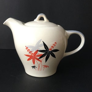 May include: White teapot with a black and red floral design. The teapot has a lid and a handle.