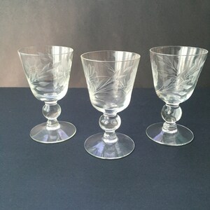 May include: Three clear glass stemmed wine glasses with an etched floral design.