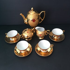 May include: A gold tea set with red accents. The set includes a teapot, creamer, sugar bowl, and four teacups and saucers.