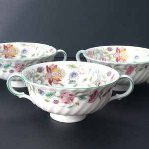 May include: Three white soup bowls with green trim and floral designs. The bowls have two handles and a pedestal base.
