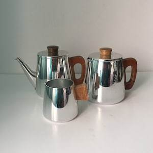 May include: A set of three silver-coloured metal teapots with wooden handles. The teapots are in different sizes and have a polished finish.