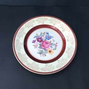 May include: A vintage floral dinner plate with a white centre, a maroon rim, and a gold-trimmed border. The centre features a bouquet of pink, purple, and yellow flowers.