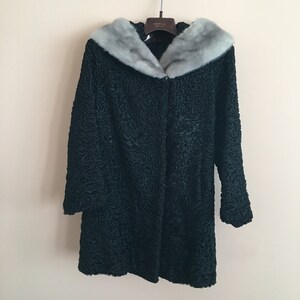 Peut inclure: Un manteau vert foncé texturé avec un col en fourrure gris clair, suspendu à un cintre en métal. Le manteau a une fermeture à bouton et des manches longues. Le manteau semble être fait d'une matière lourde, adaptée au temps froid.