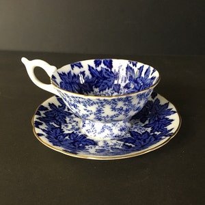 May include: A blue and white teacup and saucer set with a floral pattern. The cup has a handle and a pedestal base. The saucer has a gold rim.