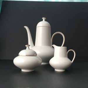 May include: A white porcelain tea set with gold trim. The set includes a teapot, creamer, and sugar bowl.