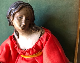 May include: A vintage wooden figurine of a woman wearing a red dress with gold trim and a lace trim. The figurine has a painted face and dark hair.